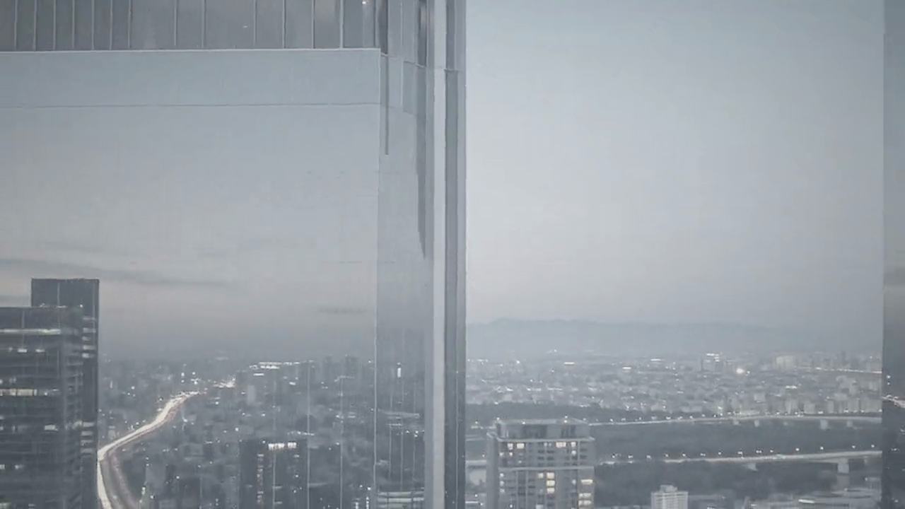夕暮れの東京。ガラス張りの高層建築の間から、眼下に街の灯りが広がる。