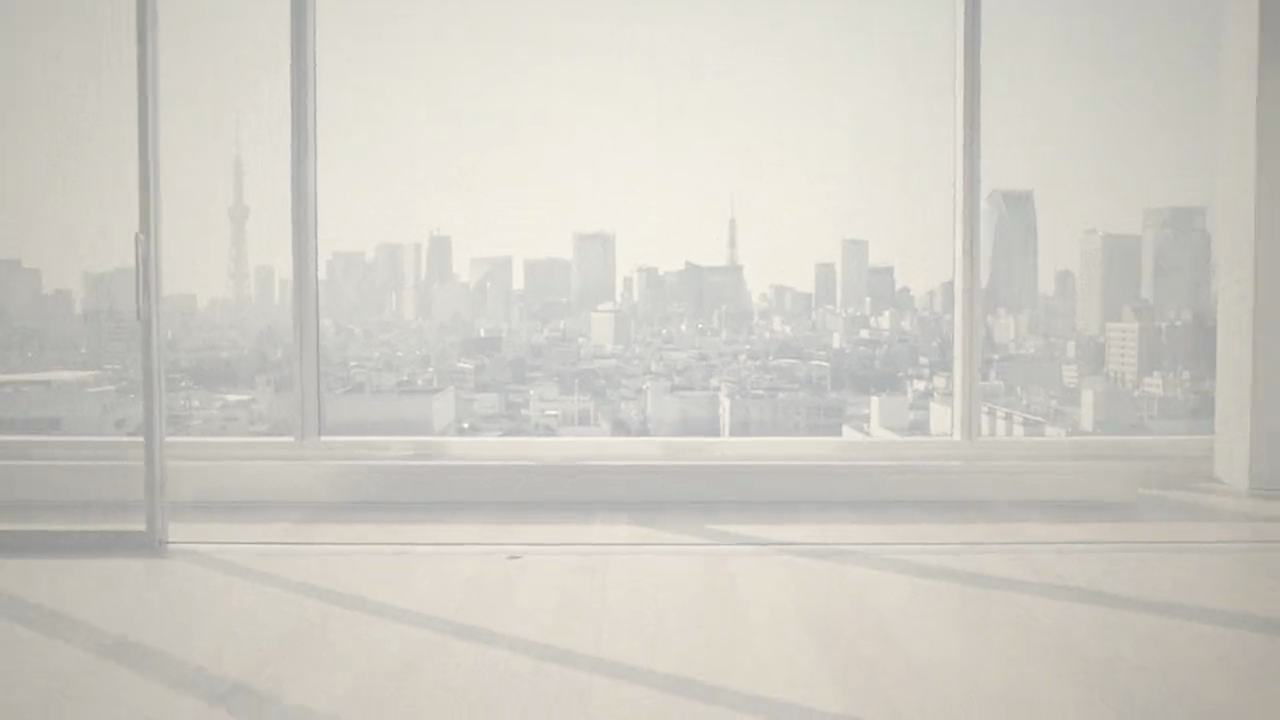 朝の光が差し込む木の床の室内と、窓の外の東京の街並み。